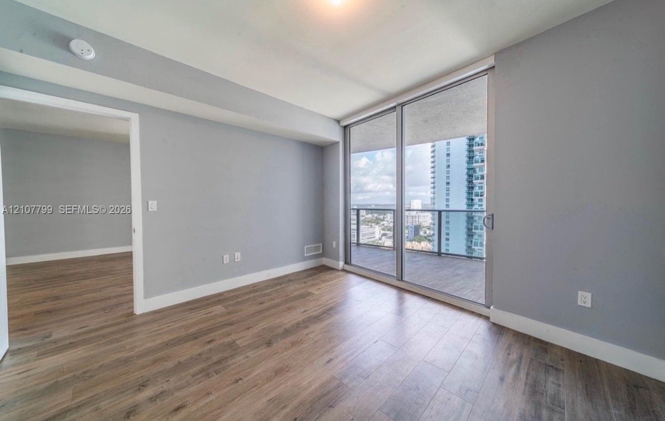 Room featuring wood-finish flooring, floor-to-ceiling glass sliding doors, and a private balcony