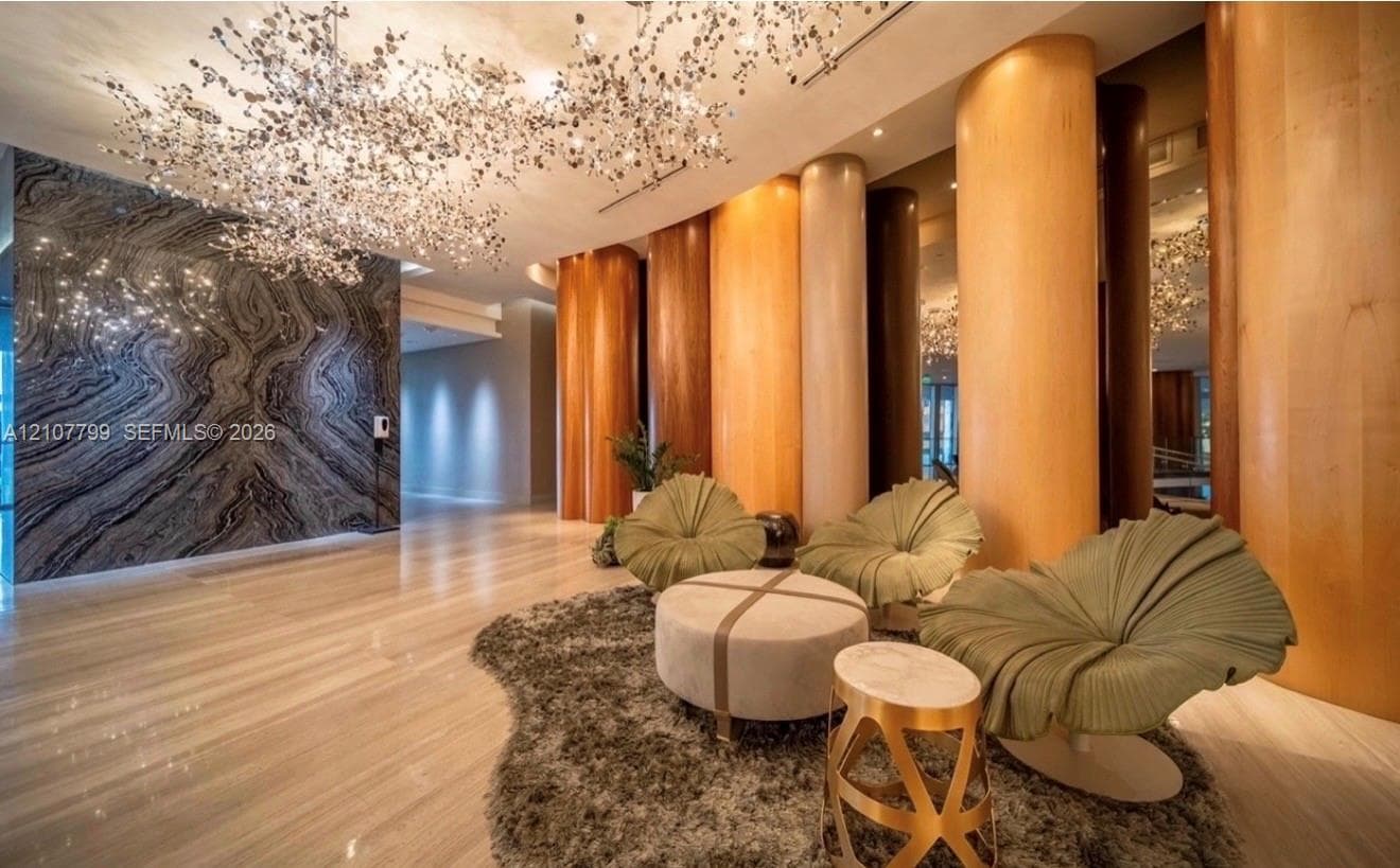 Large-scale sculptural chandelier, full-height decorative wood-paneled pillars, polished stone flooring, and expansive accent wall featuring dramatic natural veining