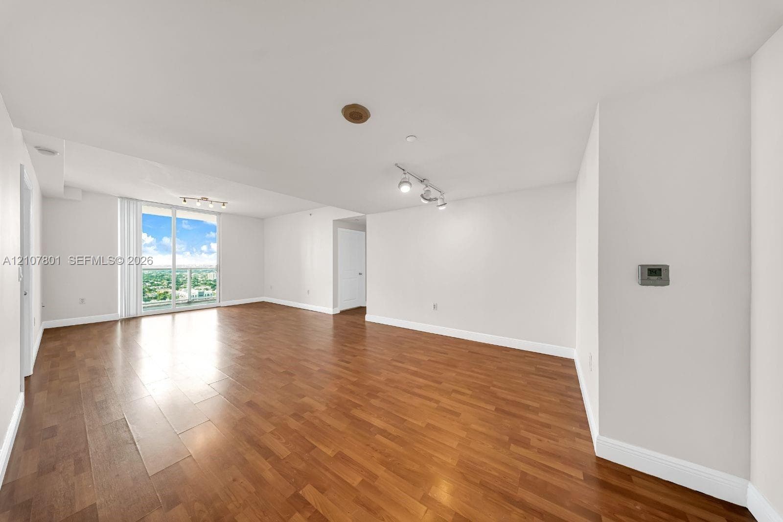 Open-concept room featuring wood-finish flooring, track lighting, a wall-mounted climate control unit, and a glass sliding door