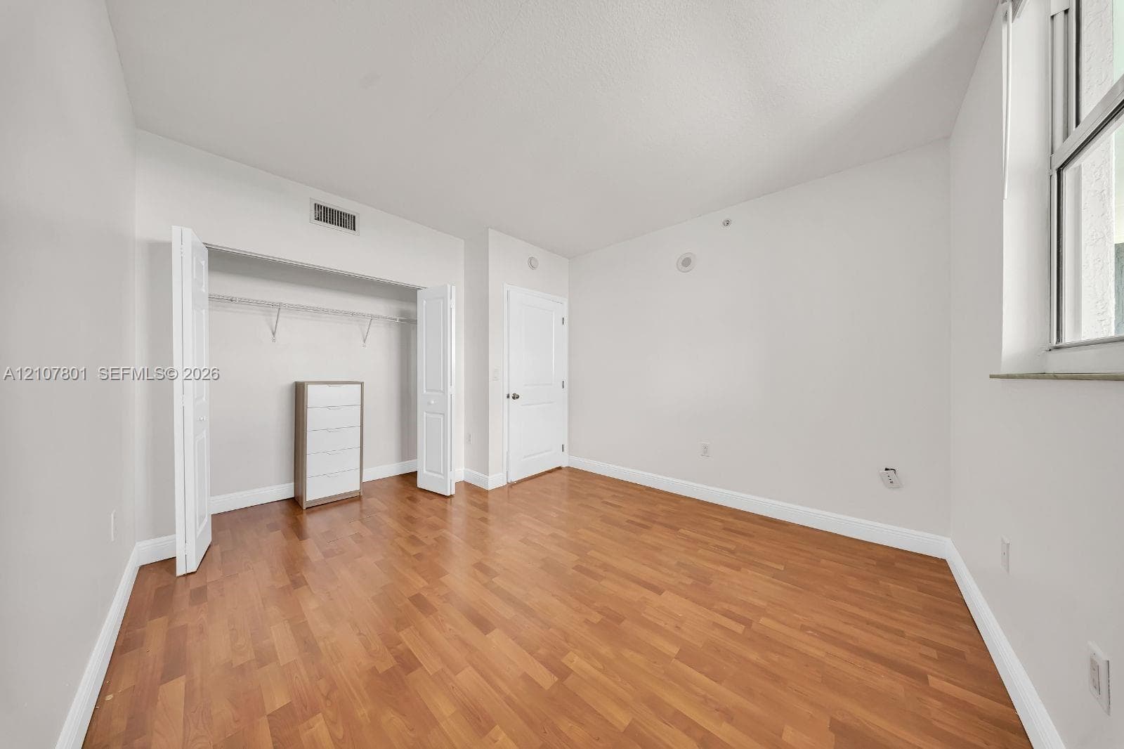 Room featuring wood-finish flooring, a neutral color palette, a window, and a built-in reach-in closet with double doors