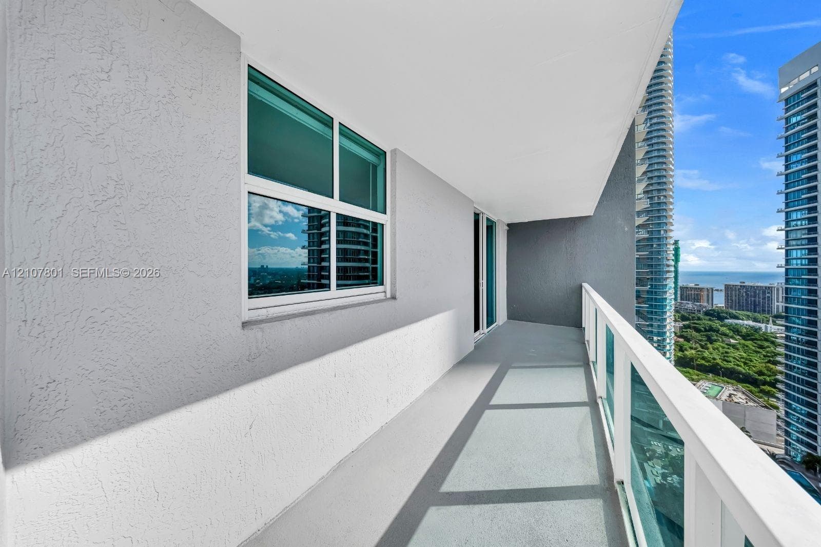 Covered balcony featuring a glass-panel railing, textured wall surfaces, and a concrete floor finish