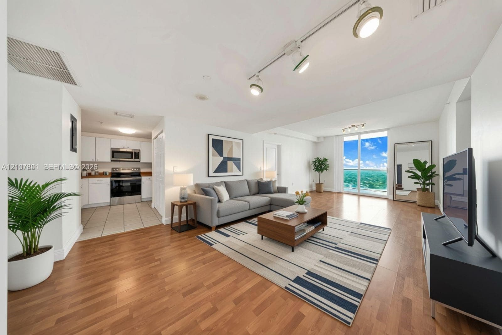 VIRTUALLY STAGED - Open-concept living space featuring wood-finish flooring, adjustable track lighting, white cabinetry, stainless steel appliances, and floor-to-ceiling glass doors
