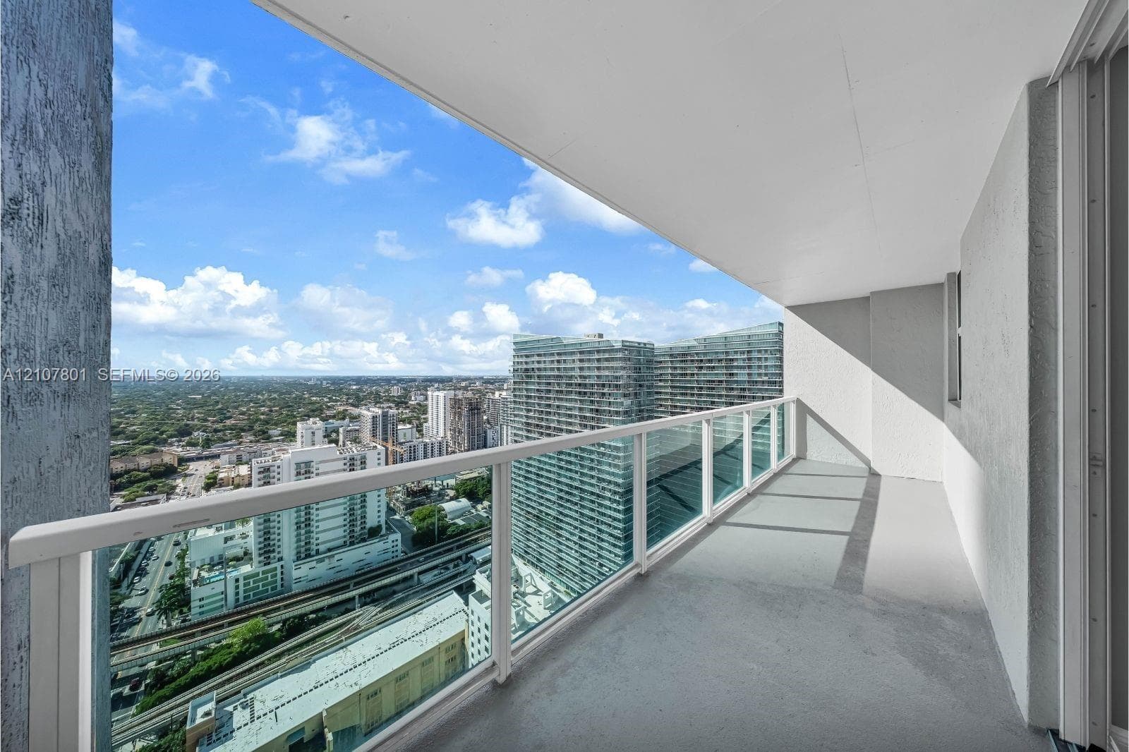Covered balcony featuring painted concrete flooring, a glass and metal railing, and high-rise urban scenery