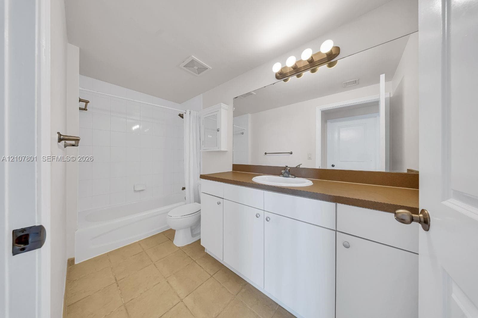 Bathroom featuring a solid-surface countertop, white cabinetry with integrated storage, a full-width wall mirror, and a tub-shower combination with tile surround