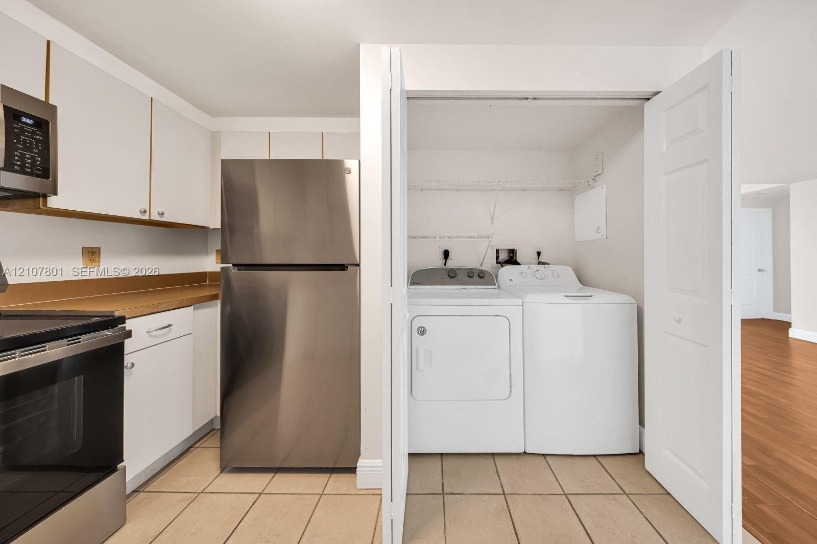 Kitchen featuring white cabinetry, stainless steel refrigerator, built-in microwave, and tile flooring, including an enclosed laundry area with bi-fold doors