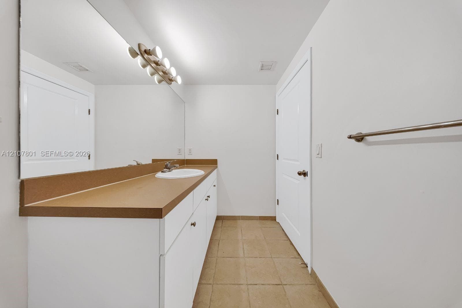 Full-width vanity with solid-surface countertop and integrated sink, expansive wall-to-wall mirror, multi-light fixture, and ceramic tile flooring