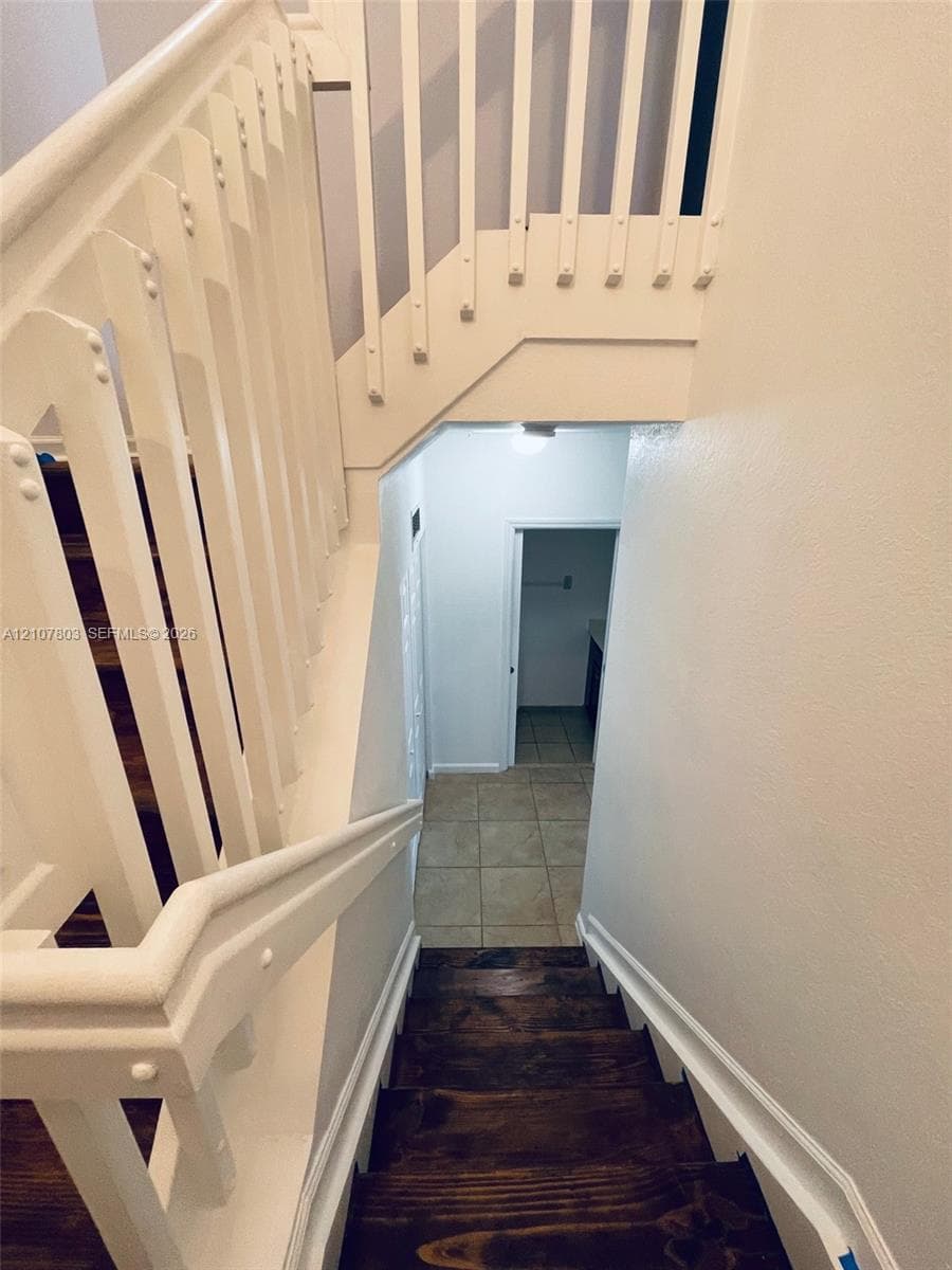 Staircase featuring stained wood treads, white-painted wood balusters, and a solid wood handrail with ceramic tile flooring at the base