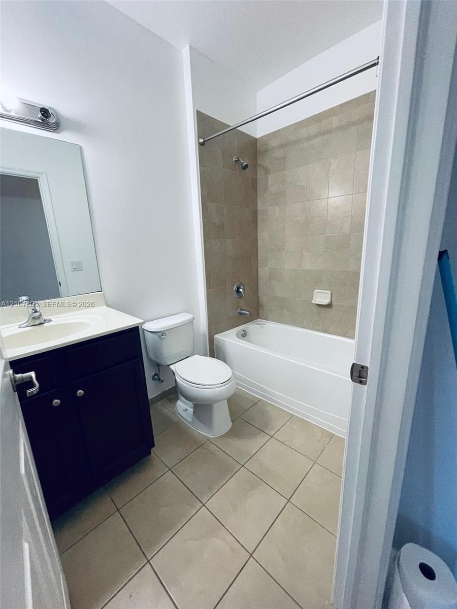Bathroom featuring a dark-finish vanity with a light-toned countertop, square-tile flooring, and a bathtub surround with neutral-tone tiling