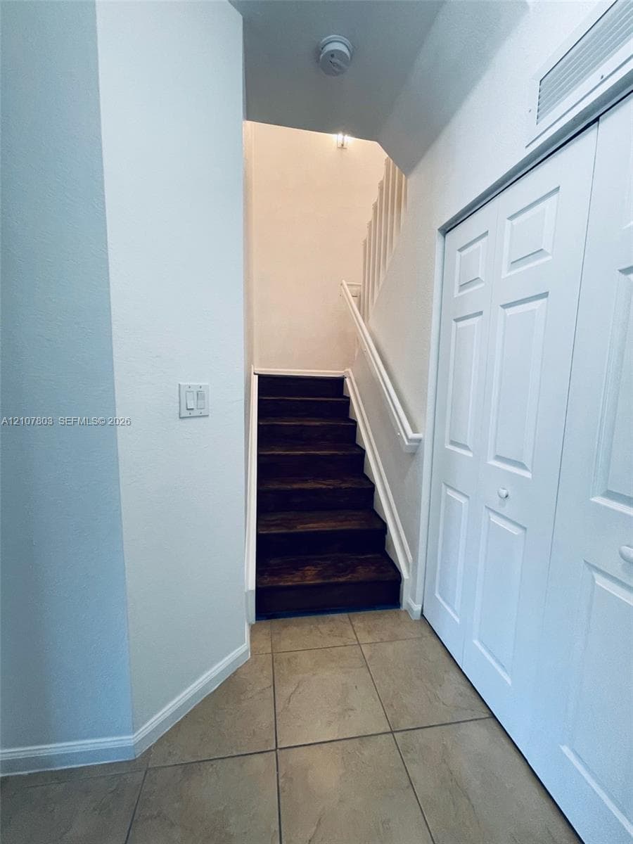 Staircase featuring wood-finish treads, white painted handrails, large-format tile flooring, and a floor-to-ceiling closet with paneled double doors