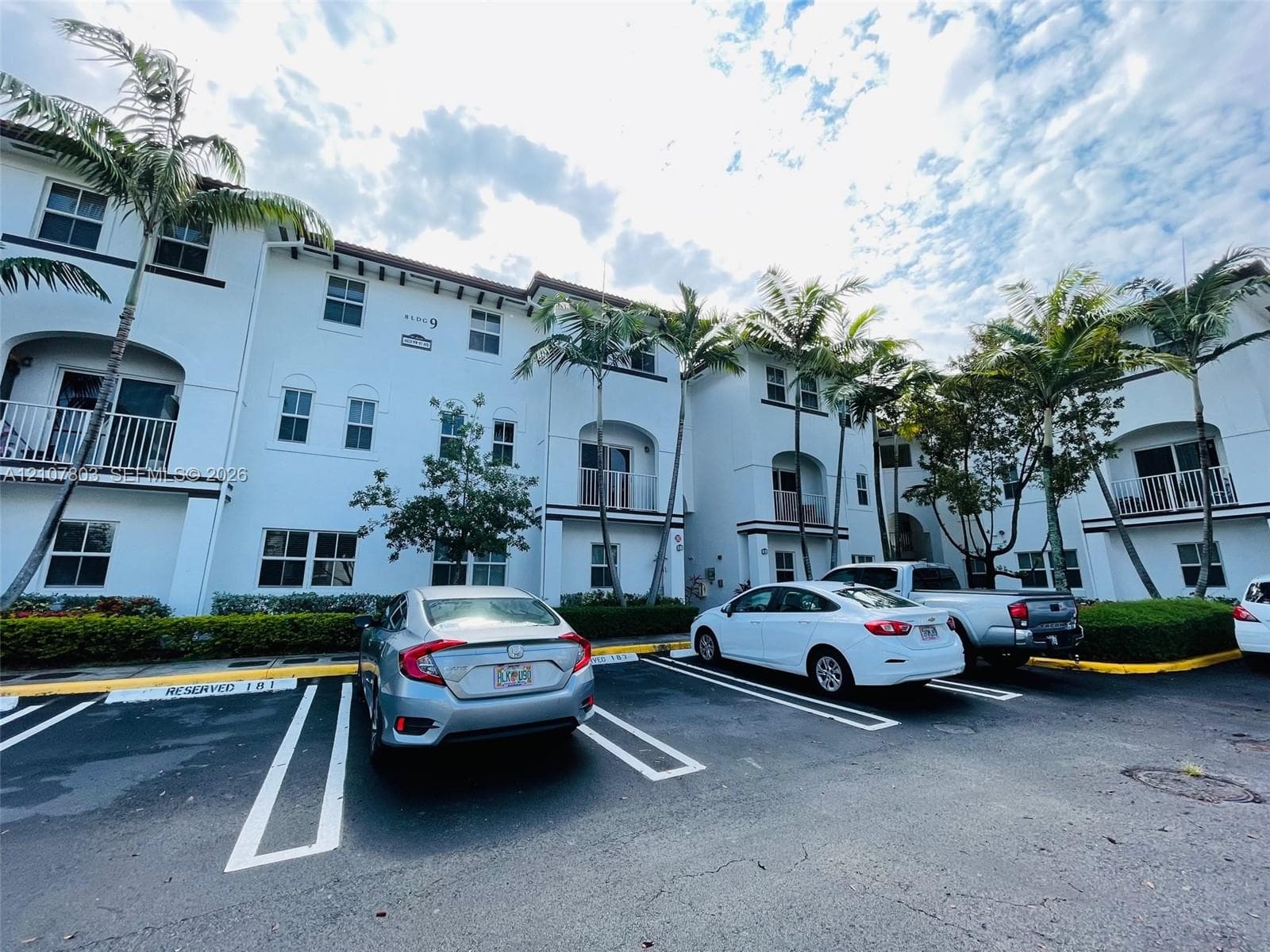 Multi-story stucco exterior featuring arched balconies, rectangular windows, and mature palm trees