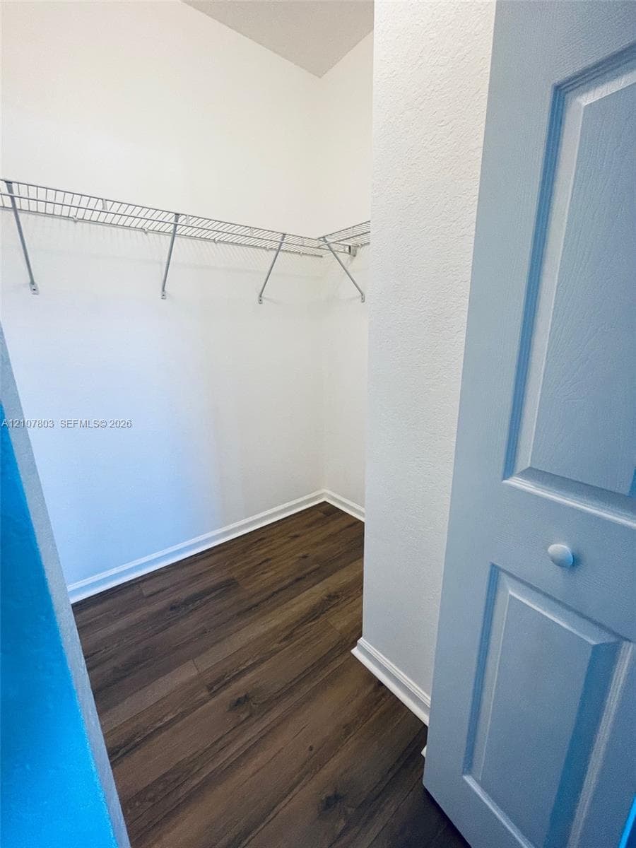 Walk-in storage space featuring wood-finish flooring, white walls, and built-in wire shelving