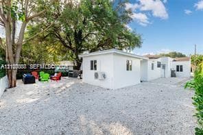 Exterior of the property featuring a white stucco facade, gravel ground cover, and mature tree canopy