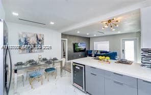 Open-concept kitchen featuring light gray flat-panel cabinetry, a white countertop island with an integrated wine cooler, recessed lighting, and large-format tile flooring
