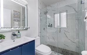 Bathroom featuring a dark blue vanity, integrated sink, LED-backlit mirror, glass-enclosed shower with large-format stone-pattern tile, and pebble-style shower floor