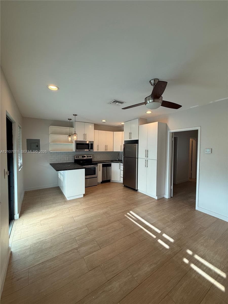 Kitchen featuring white cabinetry, wood-finish flooring, stainless steel appliances, dark countertops, and tile backsplash
