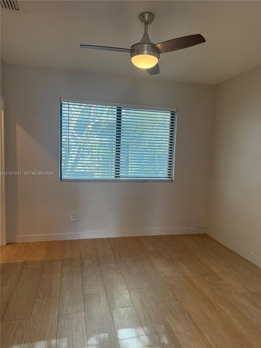 Neutral-toned room featuring wood-finish flooring, a contemporary three-blade ceiling fan with integrated lighting, and a window fitted with horizontal blinds