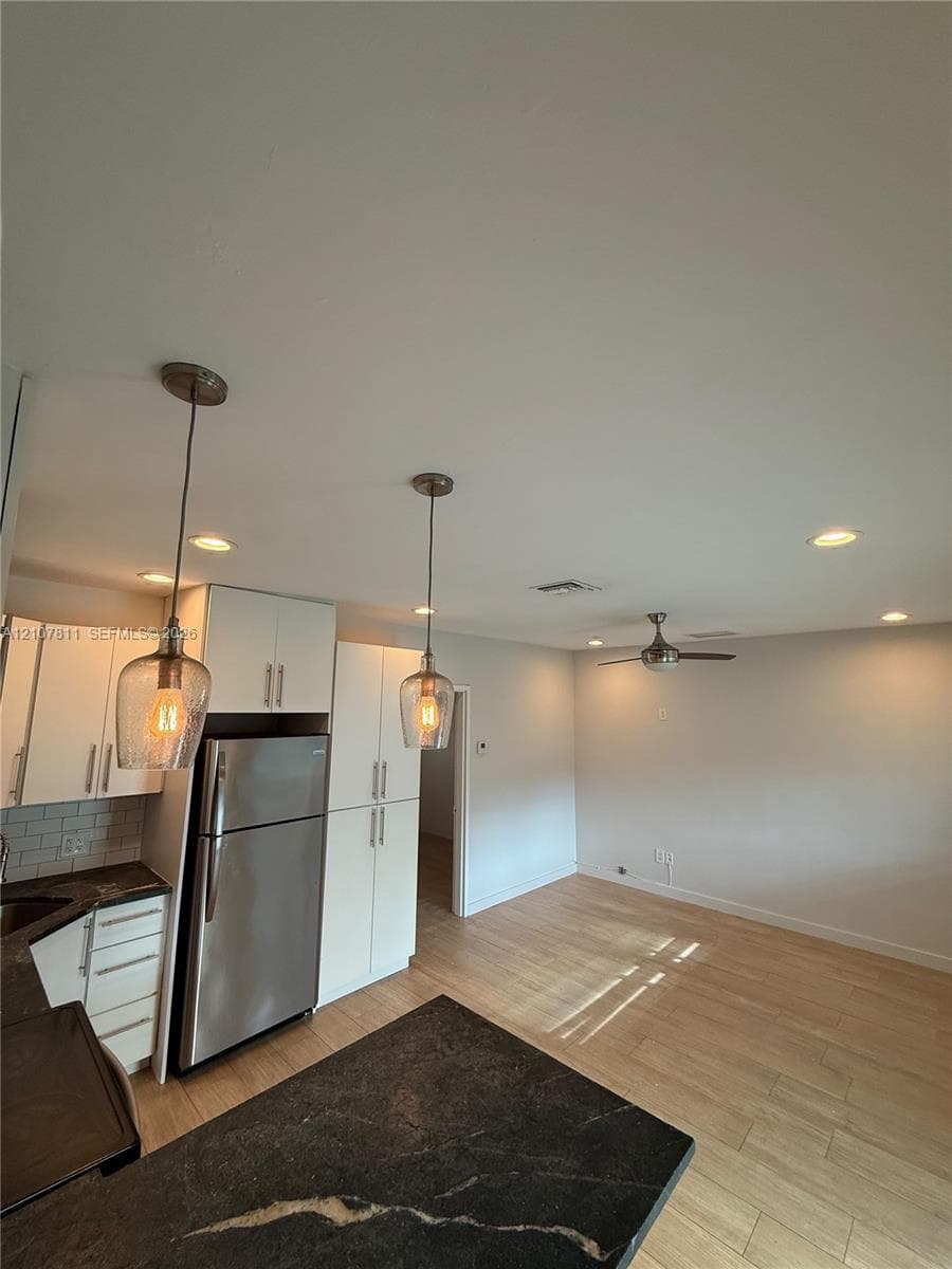 Kitchen featuring white cabinetry, stone-finish countertops, stainless steel refrigerator, glass pendant lighting, and wood-finish flooring