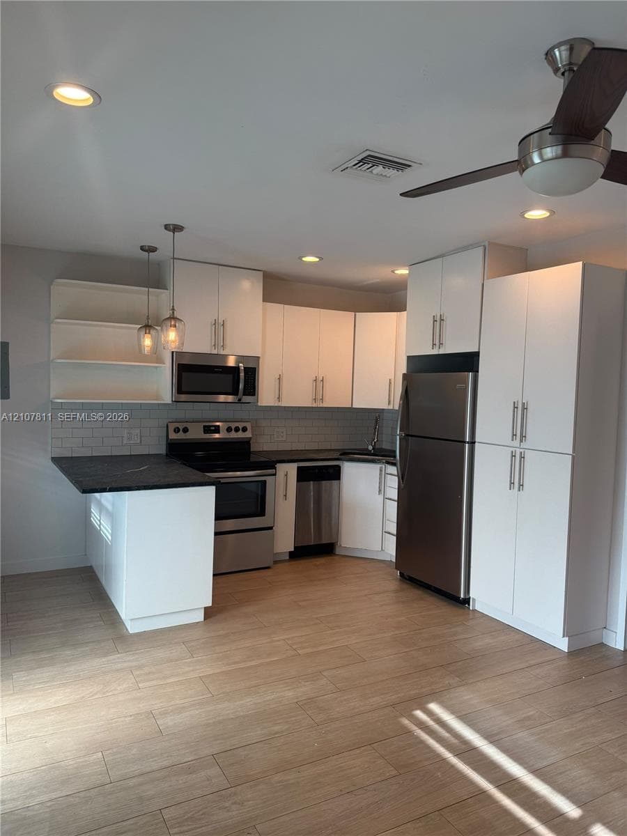 Kitchen featuring white shaker-style cabinetry, stainless steel appliances, dark stone countertops, subway tile backsplash, and wood-finish flooring