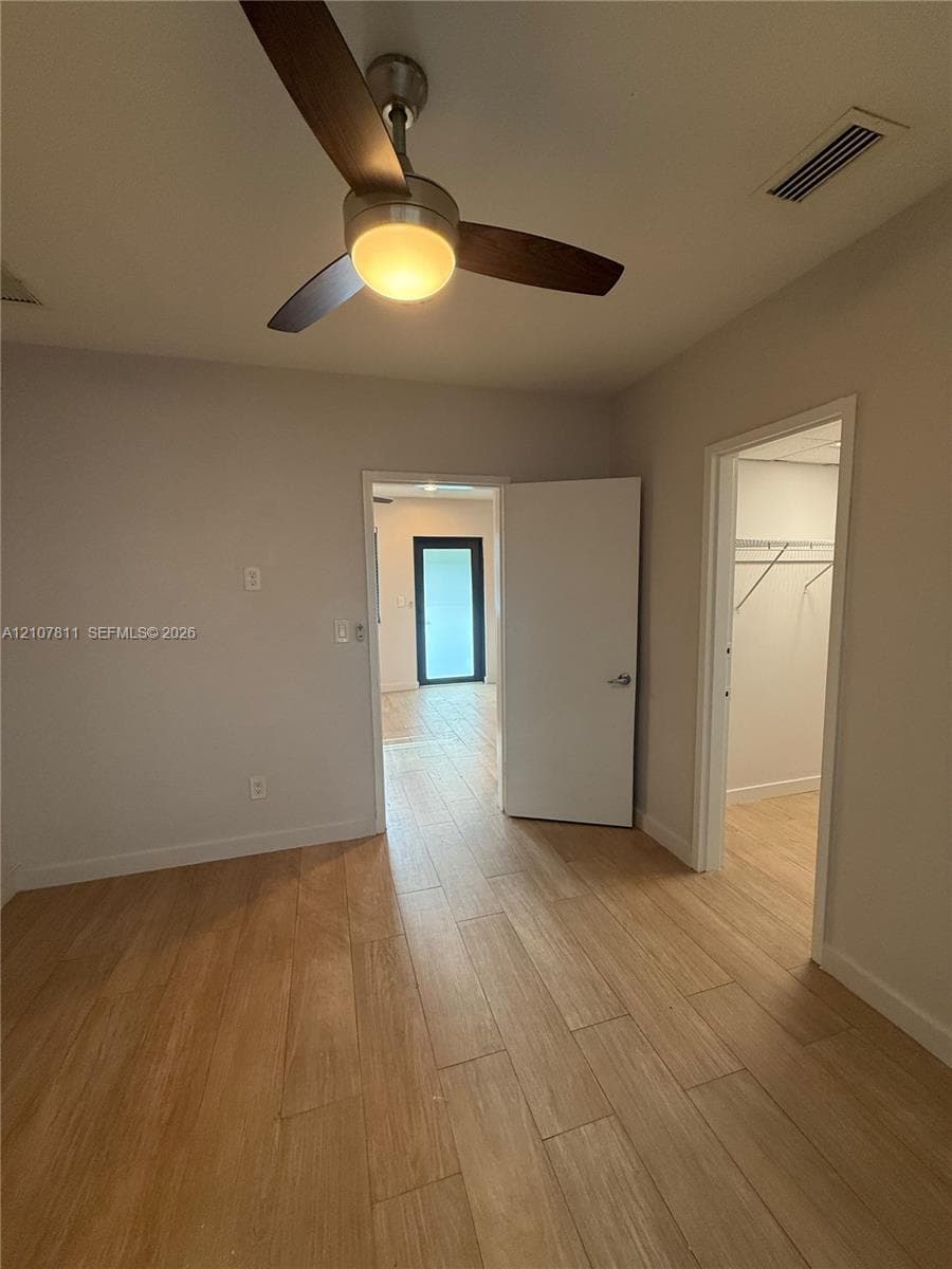 Room featuring wood-finish flooring, a ceiling fan with integrated lighting, and a walk-in closet with built-in shelving