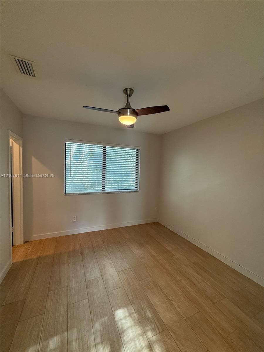 Room featuring wood-finish flooring, a neutral color palette, and a central ceiling fan with integrated lighting