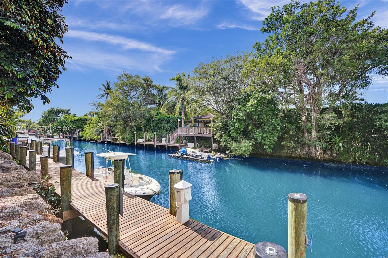Waterfront property featuring a wood-plank dock, stone retaining wall, and mature landscaping