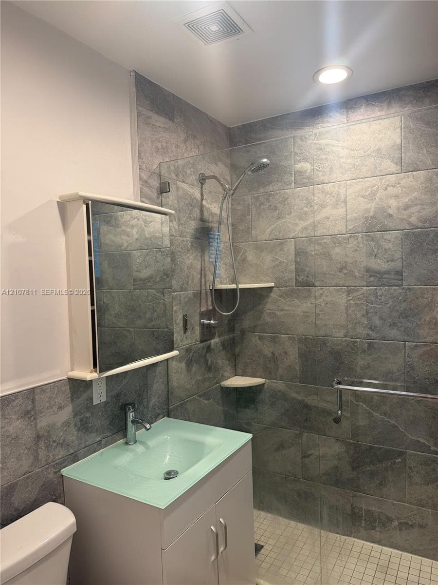 Walk-in shower featuring large-format stone-textured wall tile, a frameless glass partition, dual built-in corner shelves, and a contemporary single-handle shower system