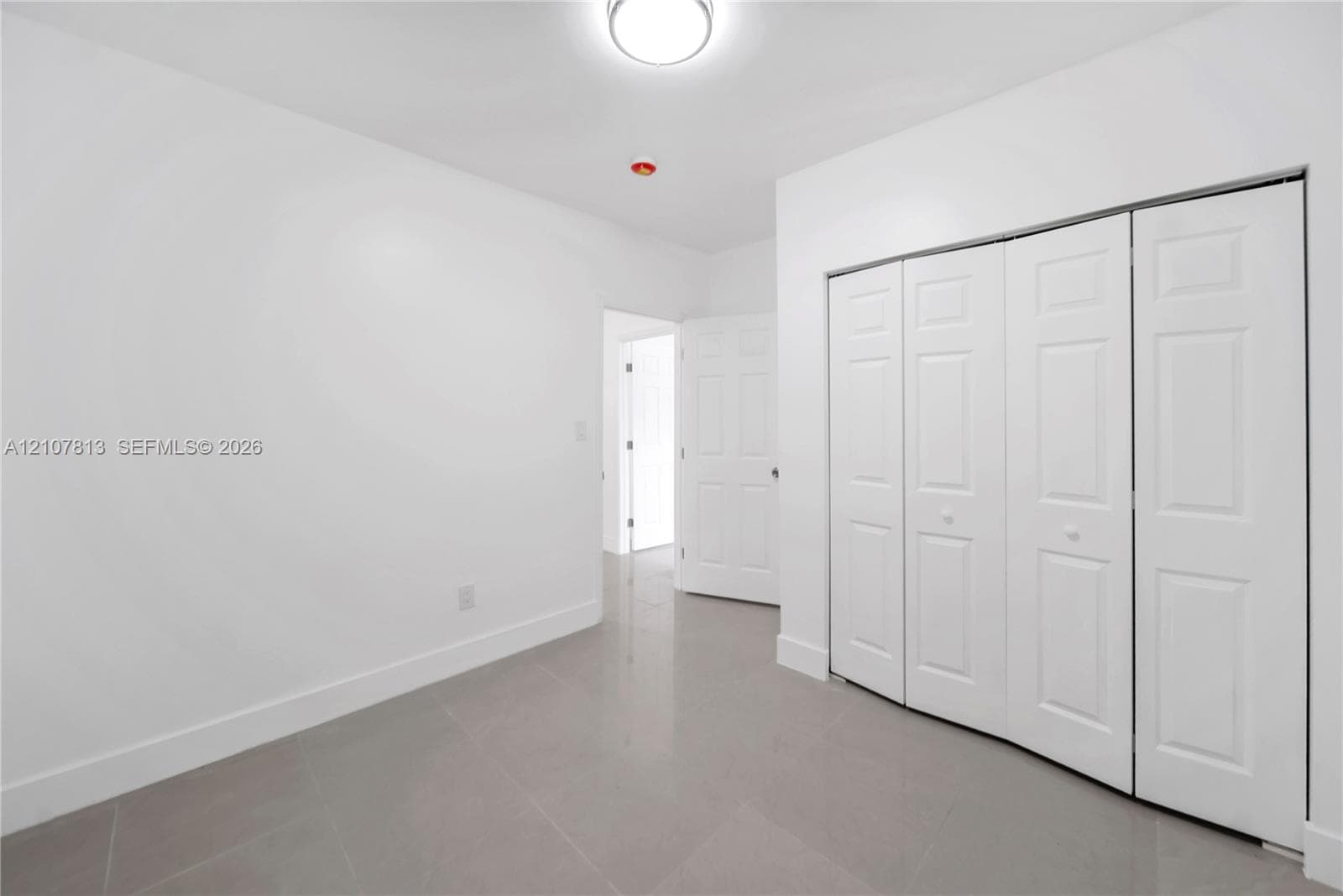 Large-format tile flooring, multi-panel bi-fold closet doors, and flush-mount ceiling lighting