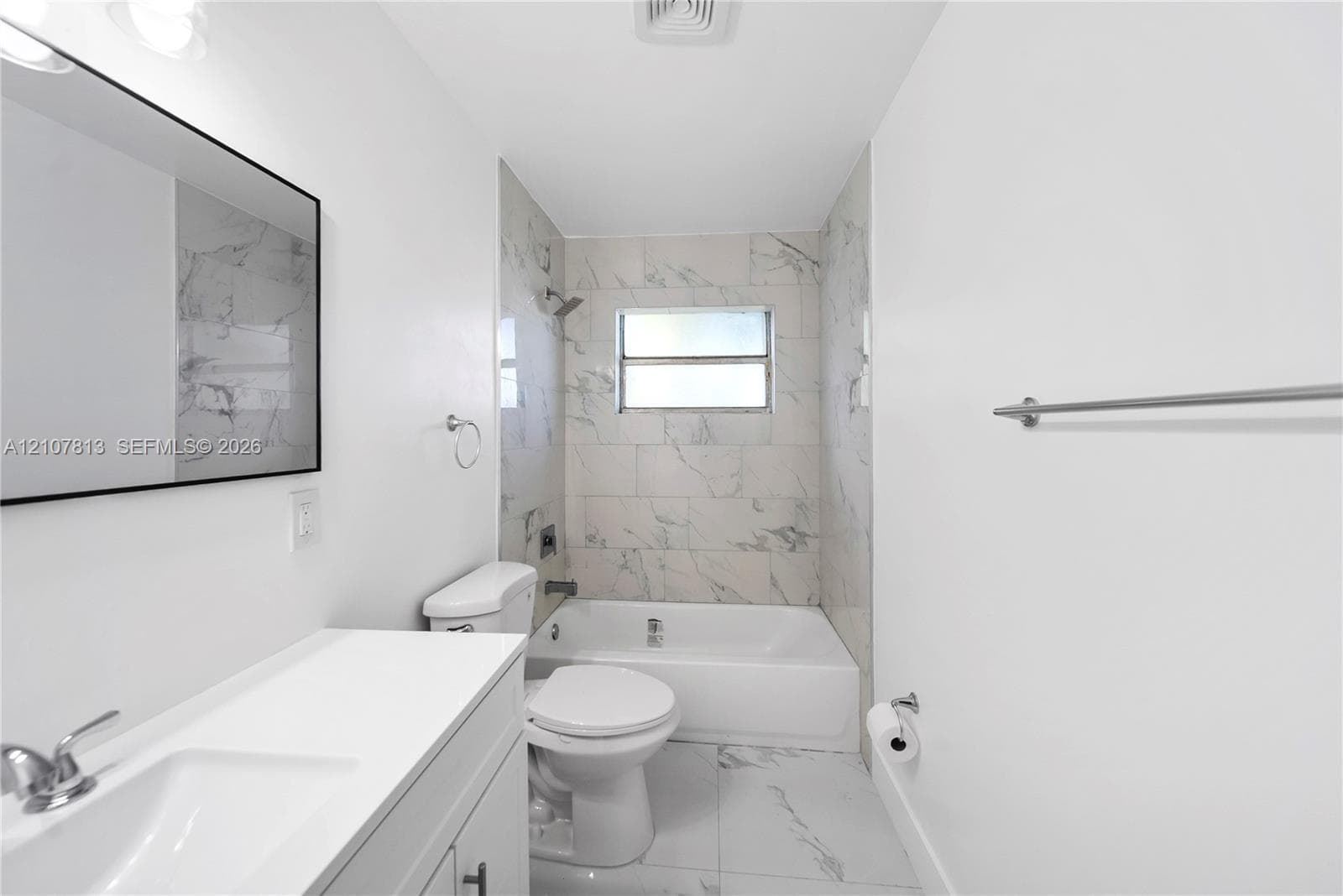 Bathroom featuring a white vanity with an integrated sink, rectangular mirror with a dark frame, and large-format tile flooring