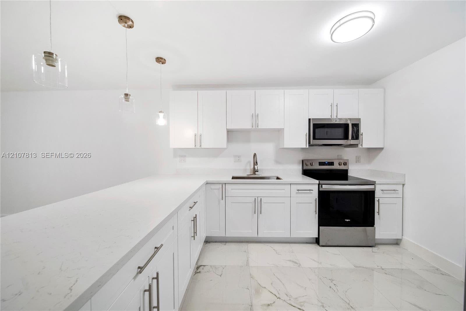 Kitchen featuring white cabinetry, quartz countertops, stainless steel appliances, pendant lighting, and large-format tile flooring