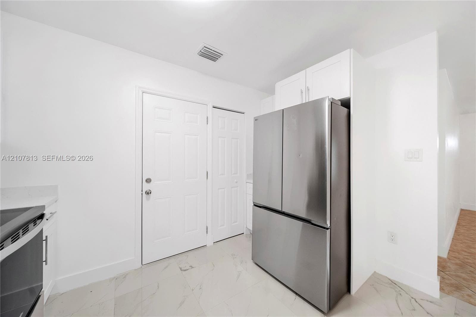 Stainless steel French-door refrigerator, white shaker-style cabinetry, large-format tile flooring, and solid-core interior doors