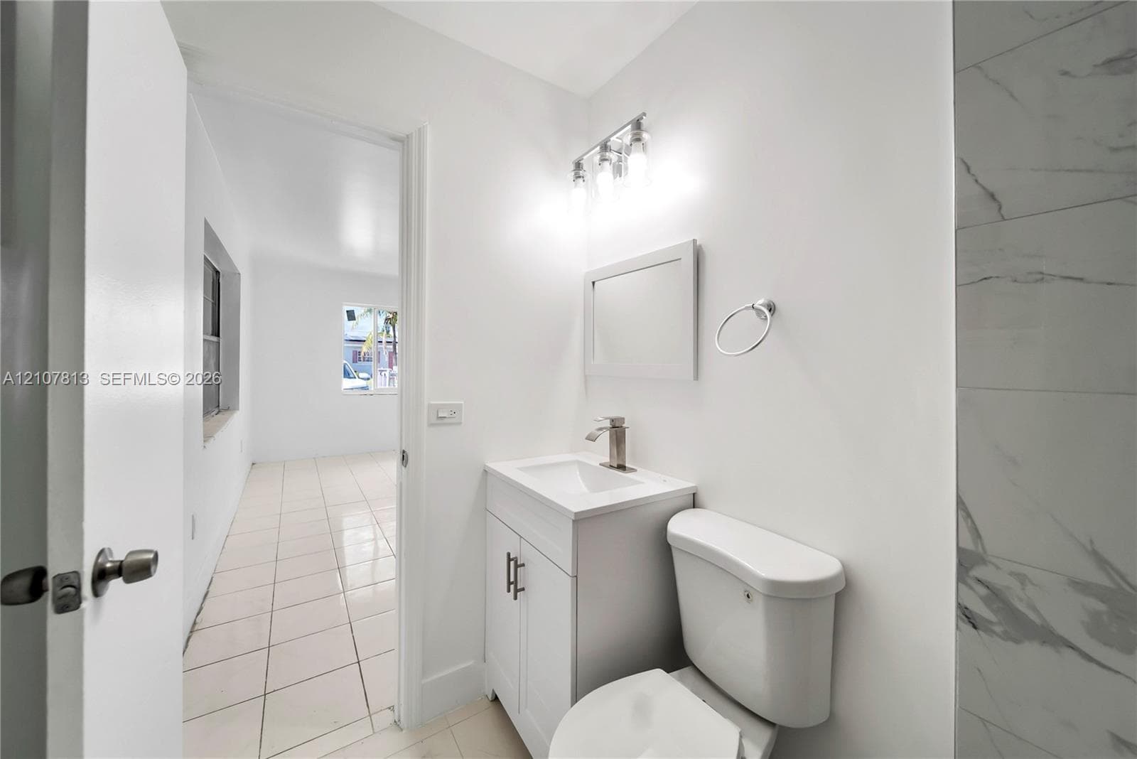 Bathroom featuring a white vanity cabinet, rectangular sink, chrome single-handle faucet, three-light fixture, and light-toned tile flooring