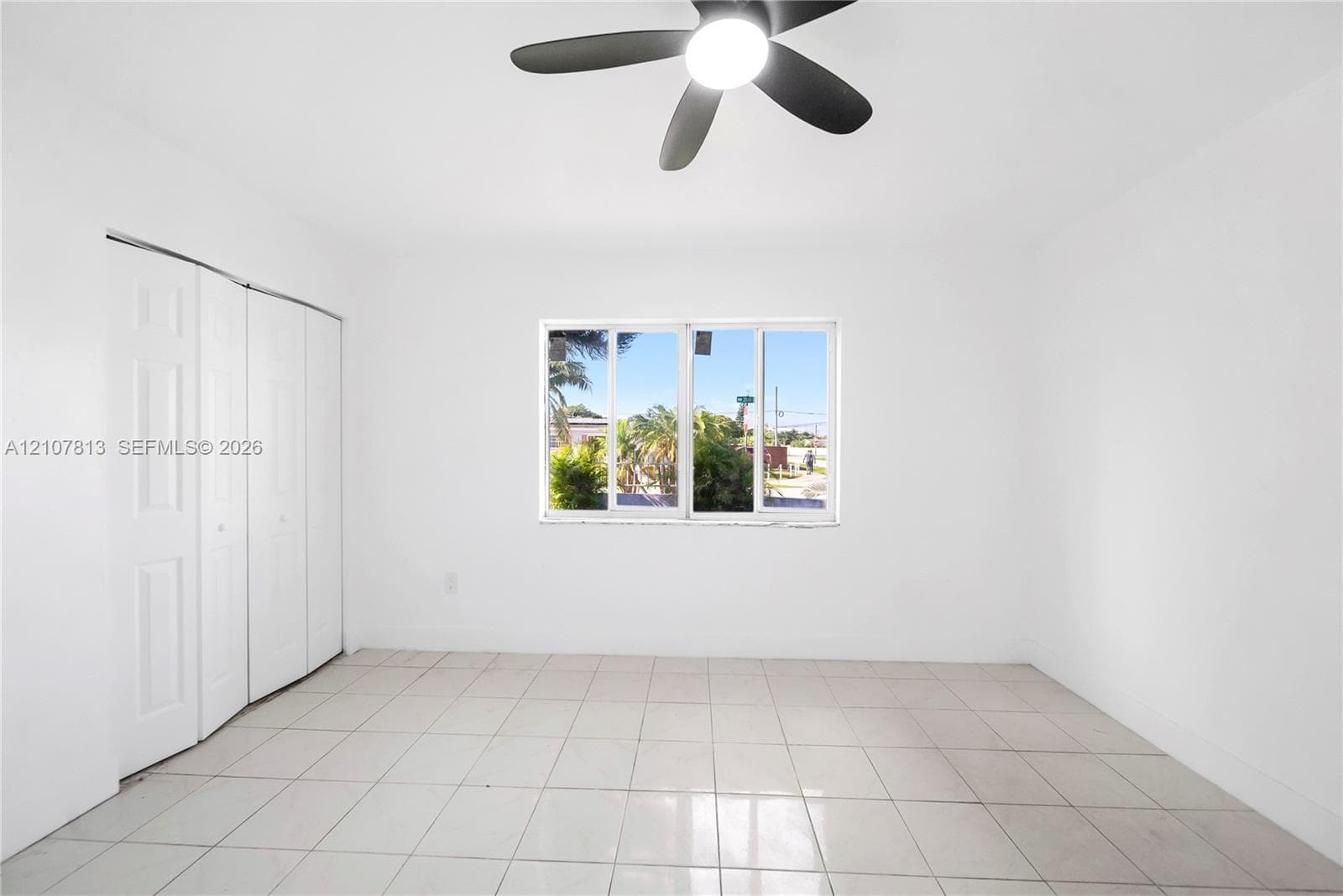 Interior space featuring neutral tile flooring, a multi-panel closet, a single window, and a ceiling-mounted fan with an integrated light fixture