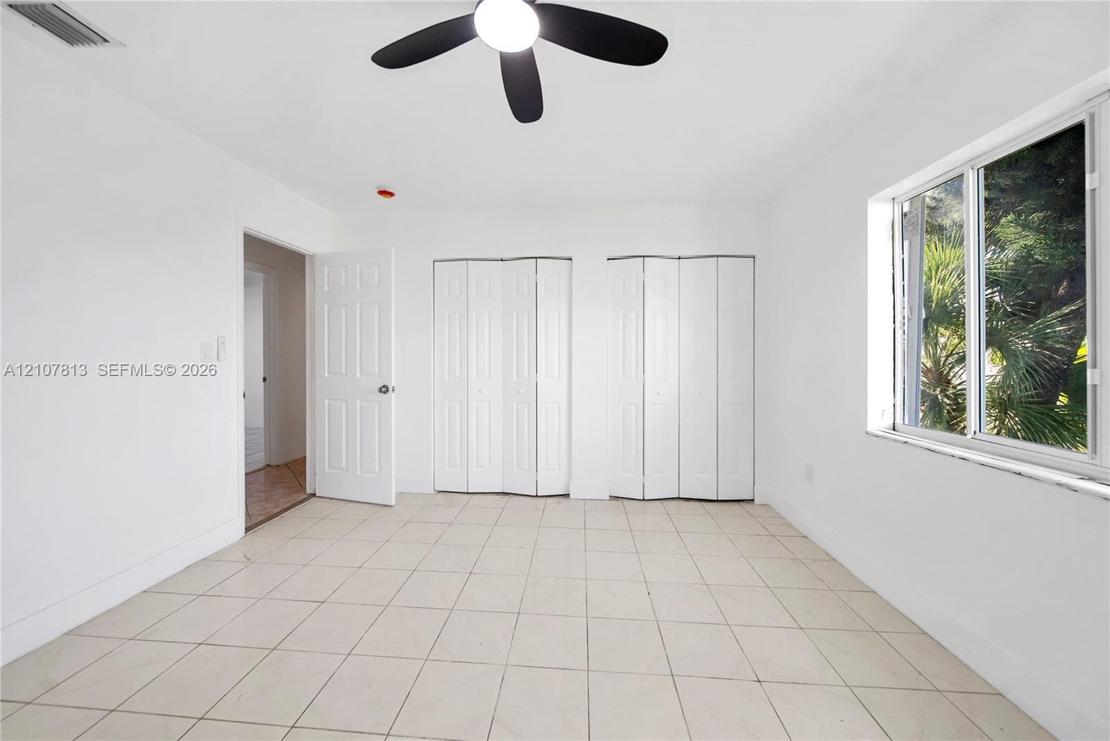 Neutral tile flooring, dual bi-fold closet doors, central ceiling fan, and multi-pane window