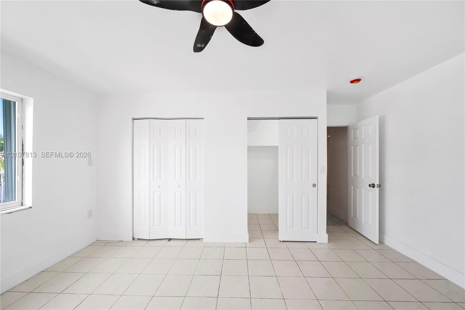 Neutral-toned ceramic tile flooring, ceiling-mounted fan with integrated lighting, dual bi-fold closet doors, and interior paneled doors