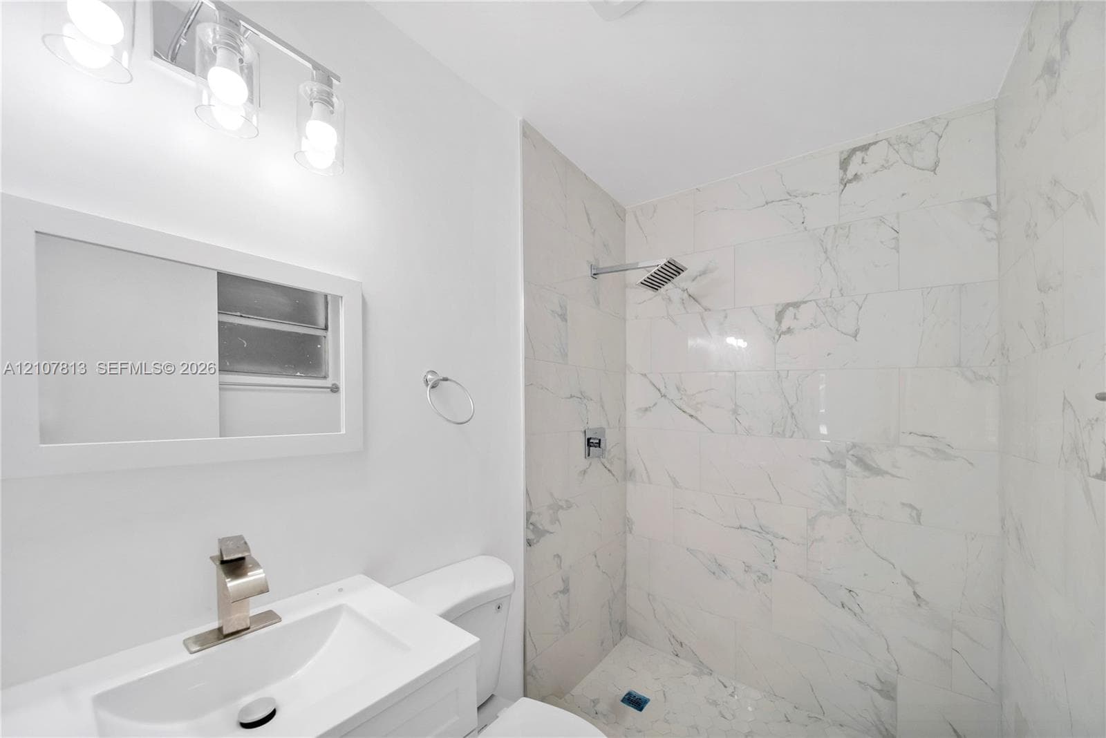 Bathroom featuring large-format stone-patterned tile shower surround, integrated sink vanity, wall-mounted light fixture, and metallic finish faucet hardware
