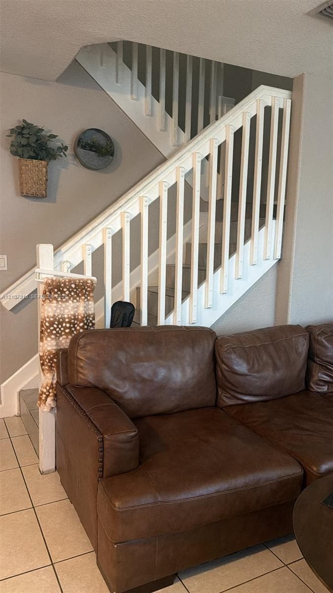 Staircase featuring white balusters, a wooden handrail, and ceramic tile flooring