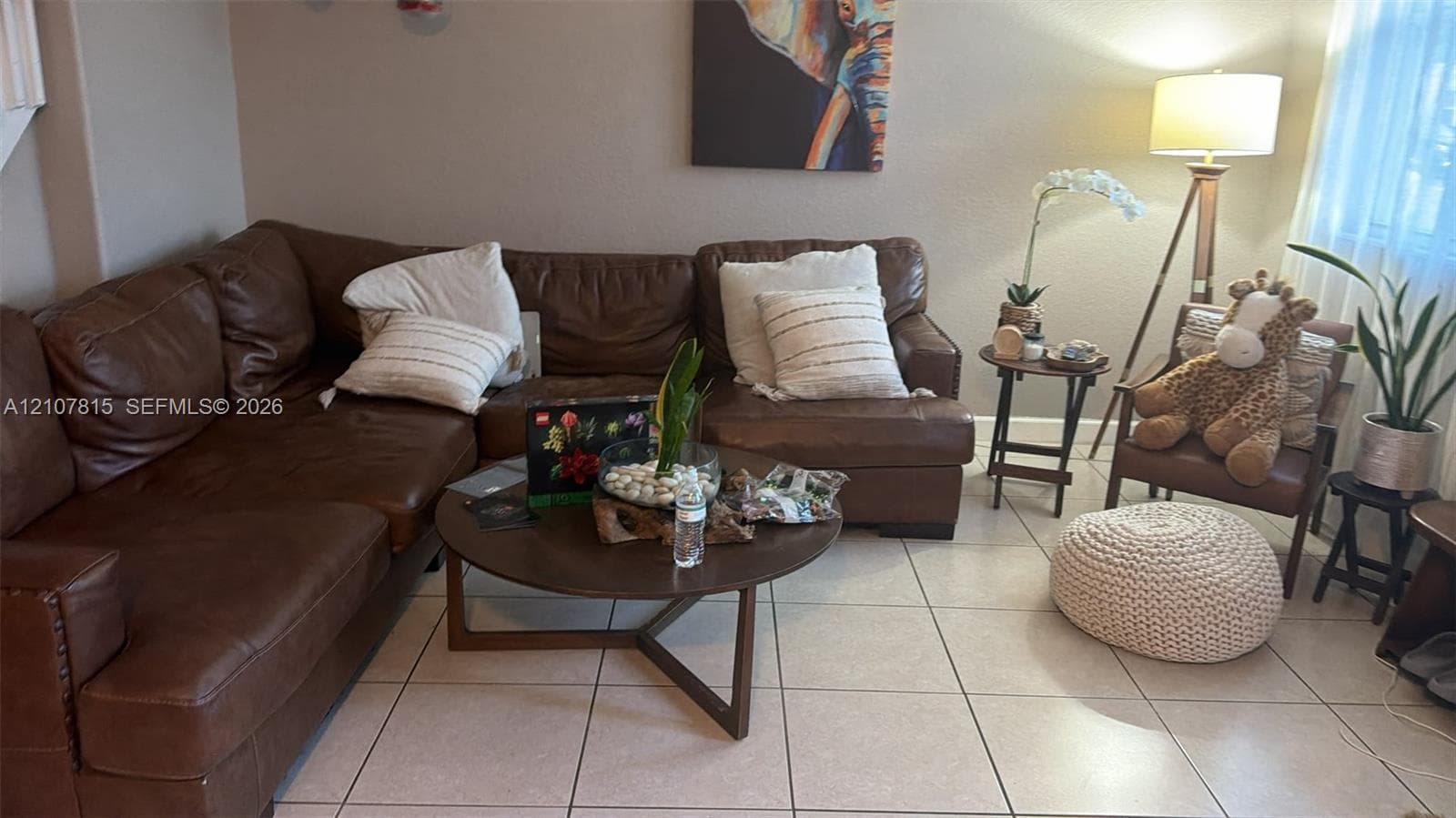 Spacious living area featuring a leather sectional sofa, tile flooring, and a round wood-finish cocktail table