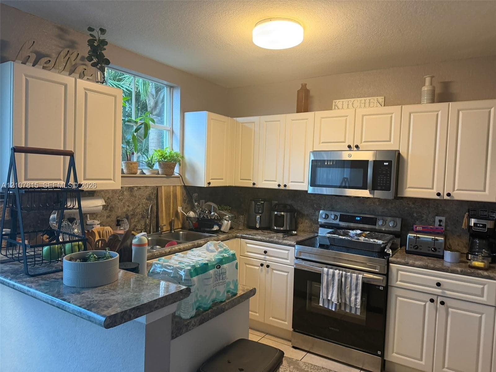 Kitchen featuring white cabinetry, stone-finish countertops, stainless steel microwave, stainless steel range, and a dual-basin sink