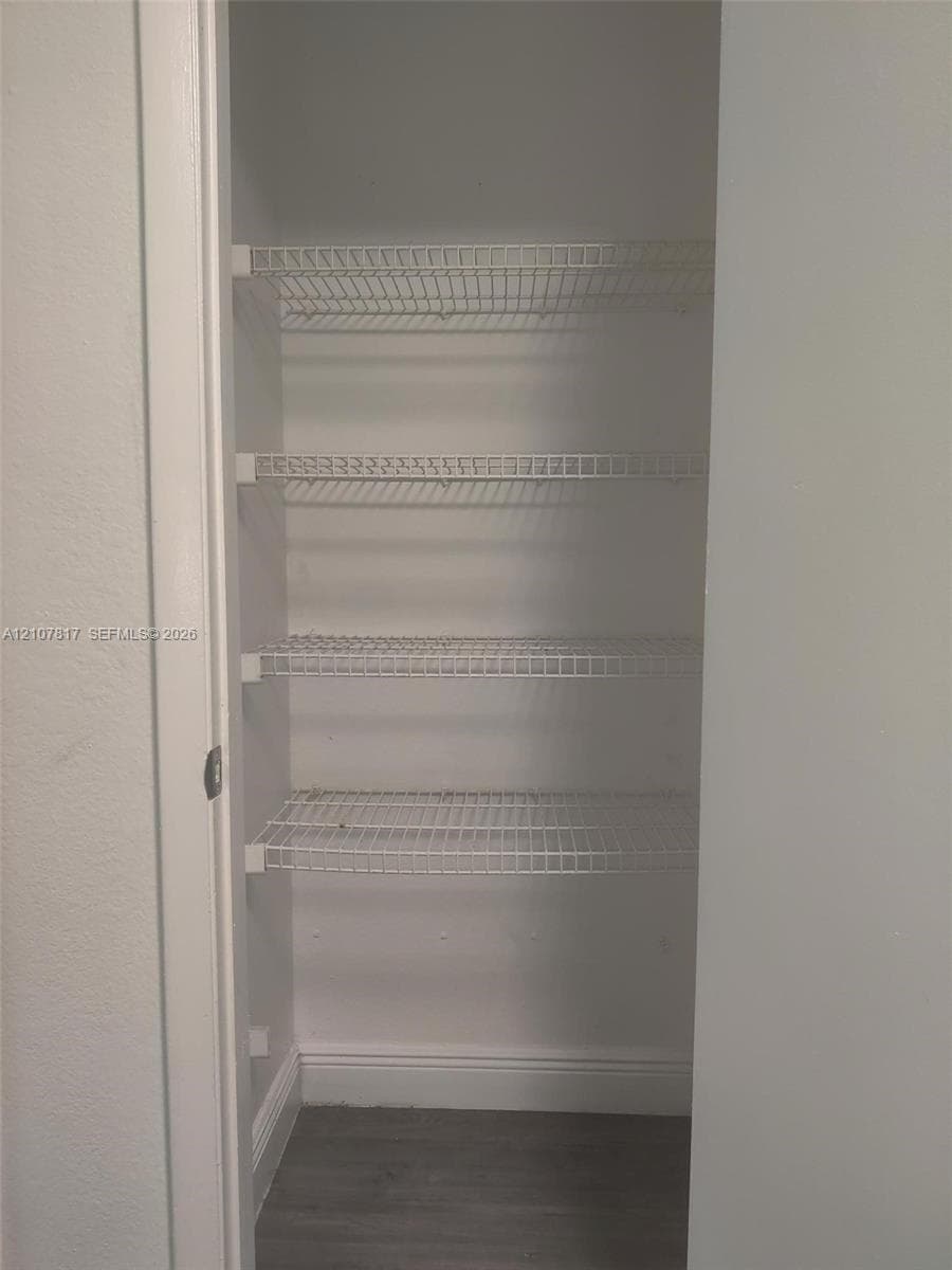 Storage closet featuring four tiers of white wire shelving and wood-finish flooring
