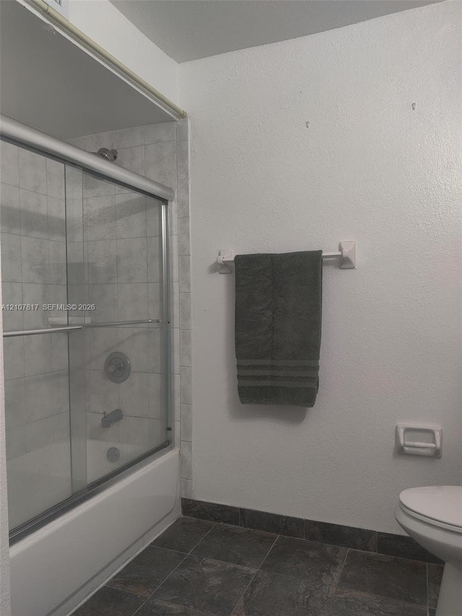 Shower-tub combination featuring a sliding glass enclosure, light-toned wall tile surround, dark slate-finish flooring, and chrome-finish plumbing fixtures