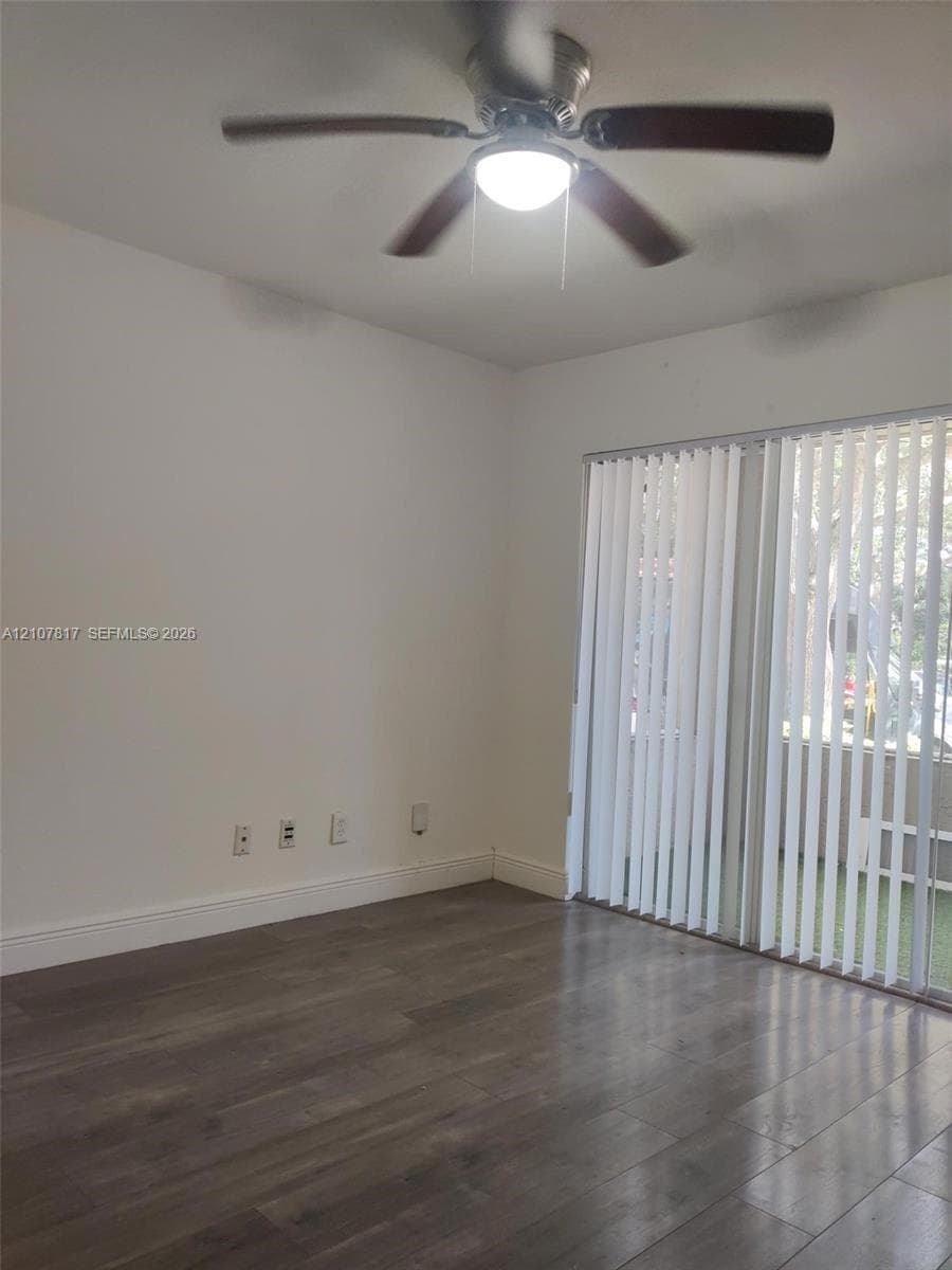 Room featuring wood-finish flooring, a ceiling fan with integrated lighting, and a large sliding glass door with vertical blinds