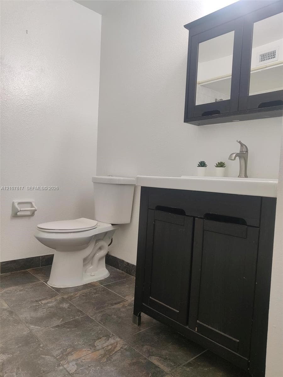 Dark-toned vanity with a rectangular sink, wall-mounted medicine cabinet, metal faucet, and stone-finish floor tiling