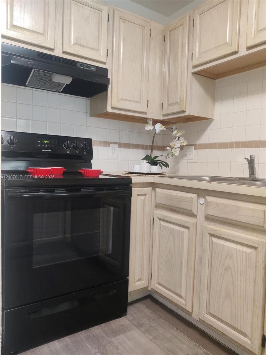 Kitchen featuring light-finish cabinetry, black freestanding range, matching black range hood, tiled backsplash, and wood-finish flooring