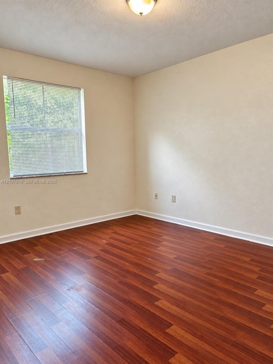Room featuring wood-finish flooring, neutral-tone wall finishes, and a single-pane window with integrated blinds