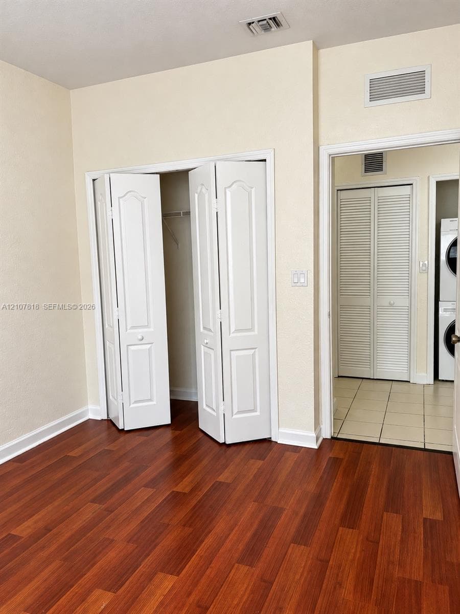 Room featuring wood-finish flooring, dual bi-fold closet doors, and tile flooring within the secondary space