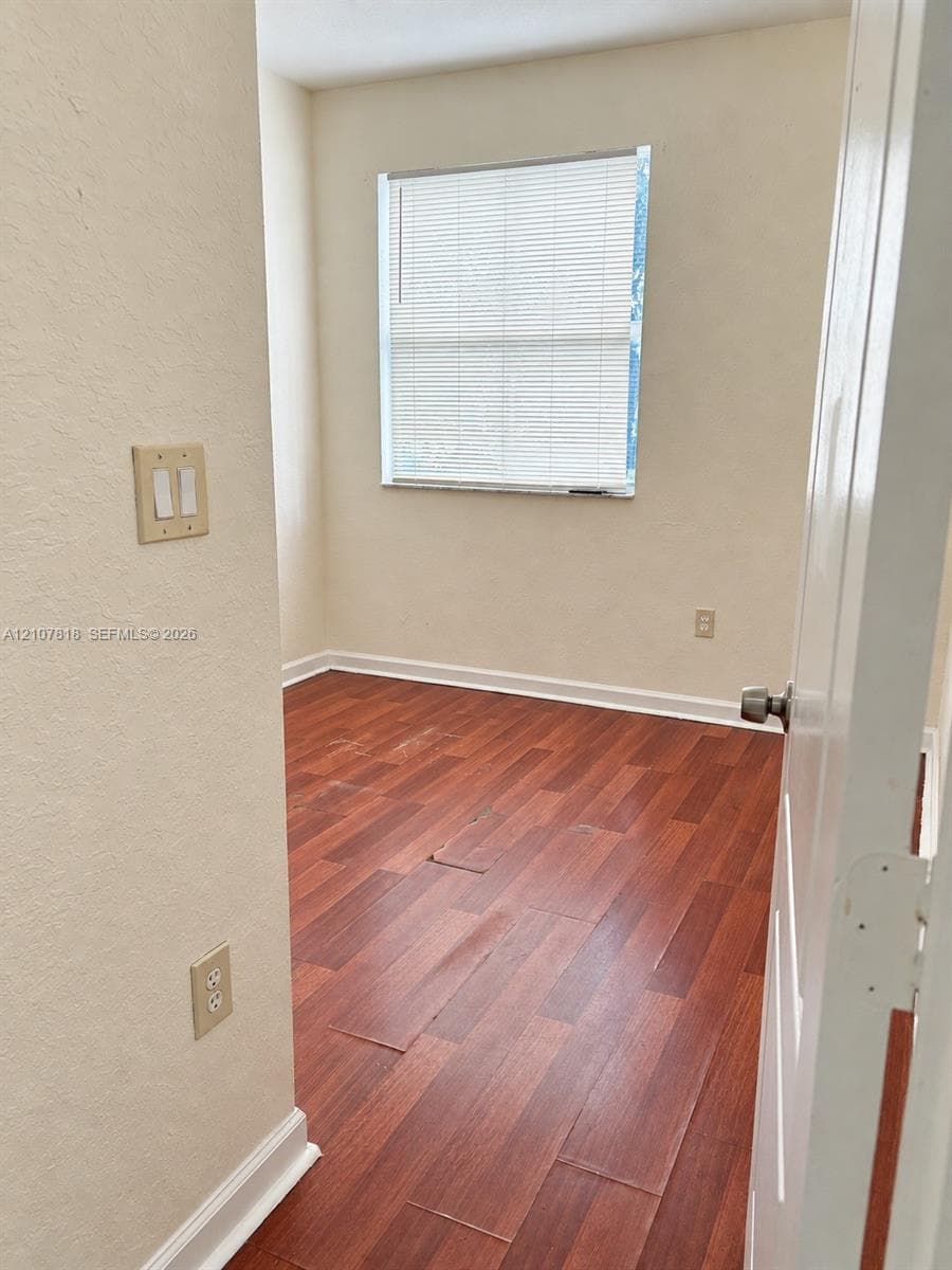 Room featuring wood-finish flooring, neutral-toned walls, and a single-pane window with installed blinds