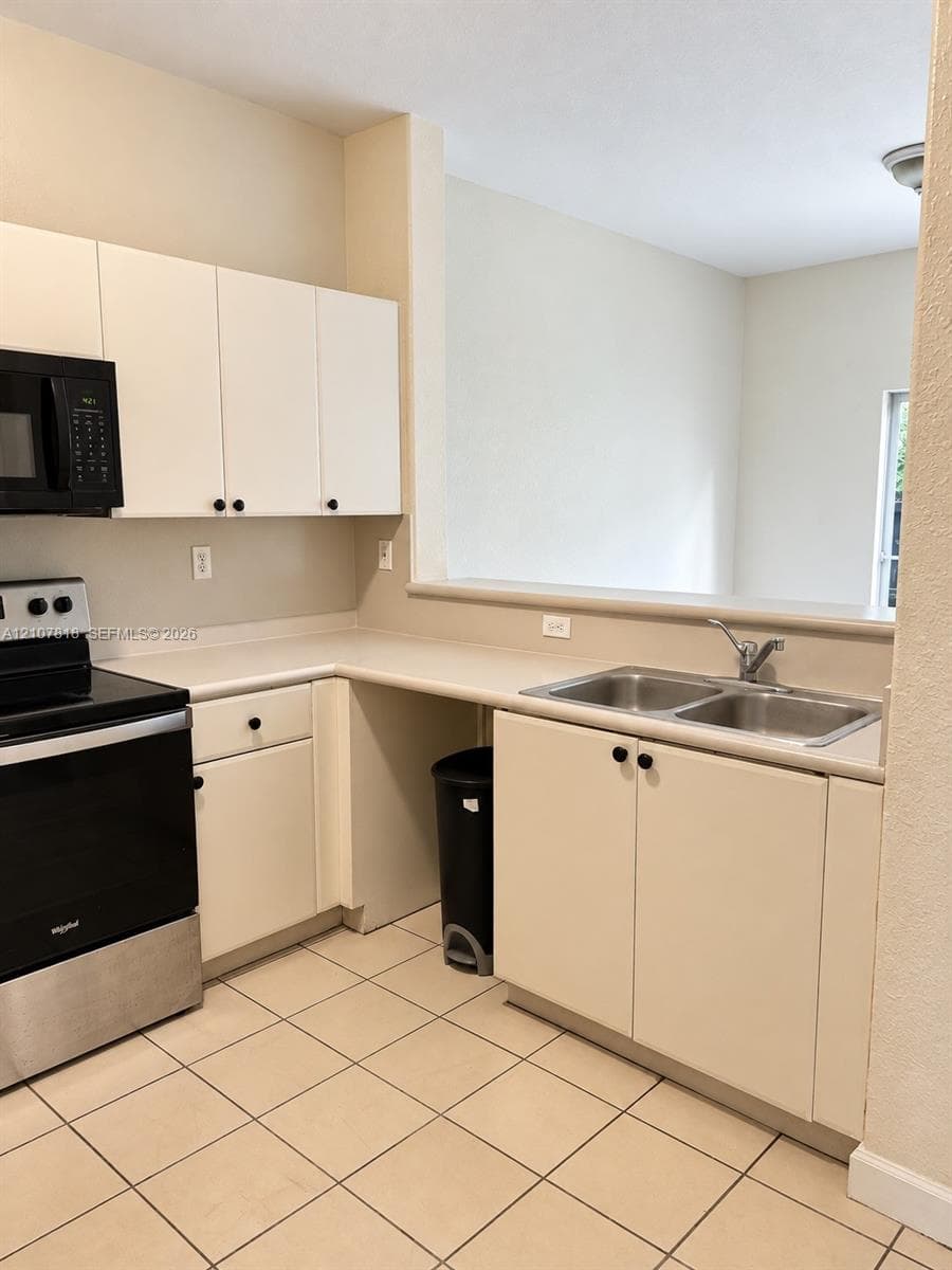 Kitchen featuring white cabinetry, dual-basin stainless steel sink, solid-surface countertops, black finish appliances, and ceramic tile flooring