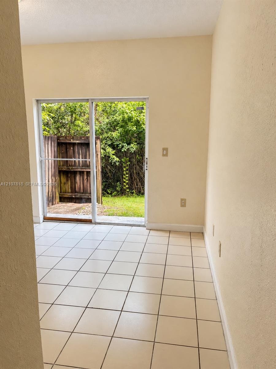 Interior space featuring large-format ceramic tile flooring and a sliding glass door providing access to a private exterior patio area enclosed by a wooden privacy fence