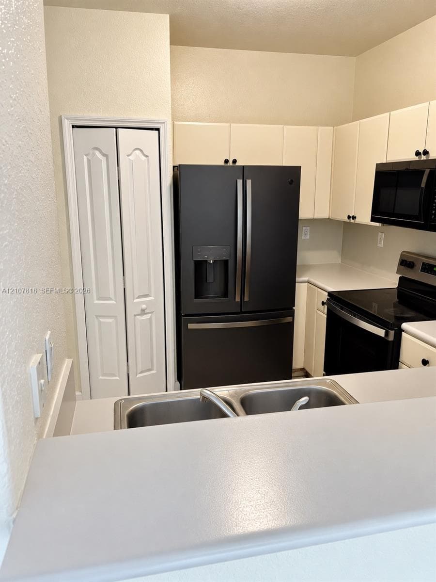 Kitchen featuring off-white cabinetry, black finish appliances, a dual-basin stainless steel sink, solid-surface countertops, and a full-height pantry with bi-fold doors