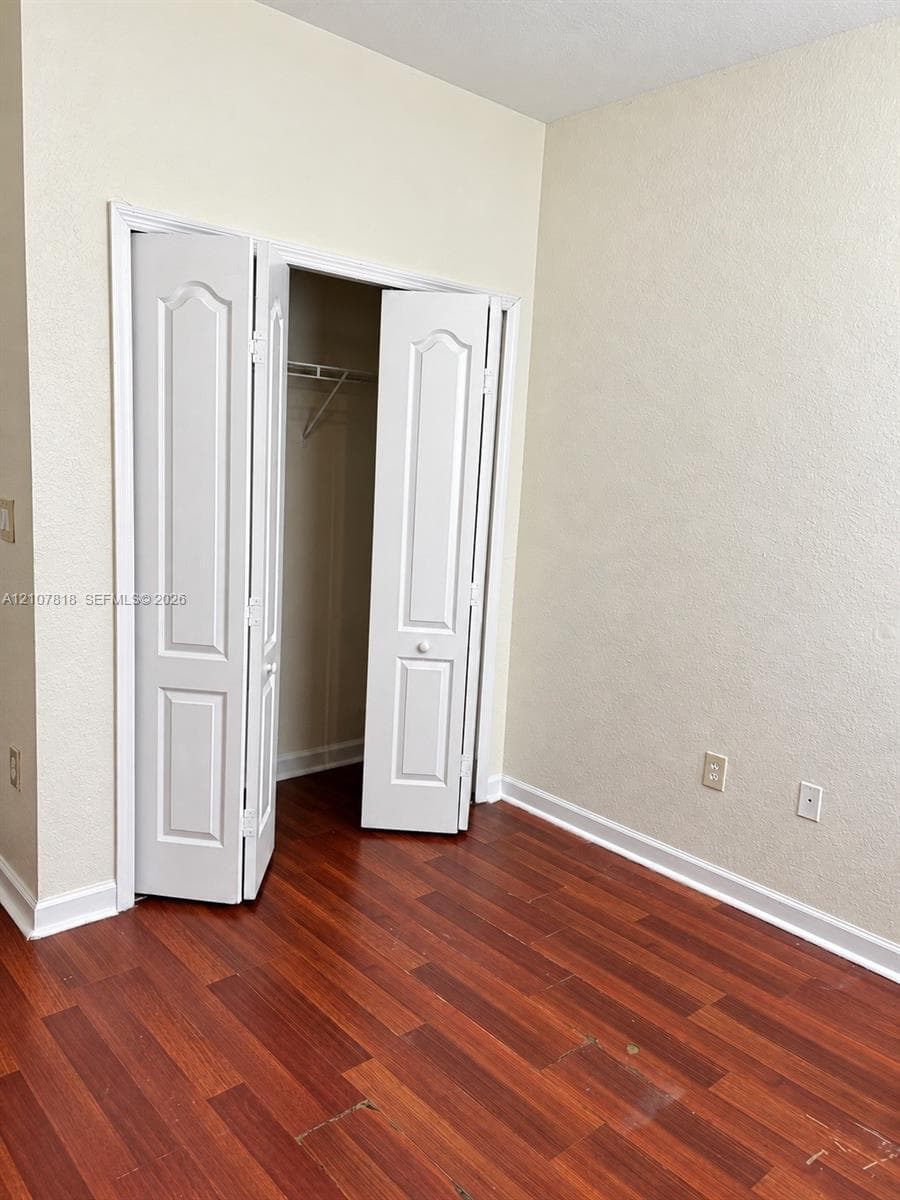 Wood-finish flooring, neutral wall paint, and a built-in closet featuring white paneled bifold doors and wire shelving
